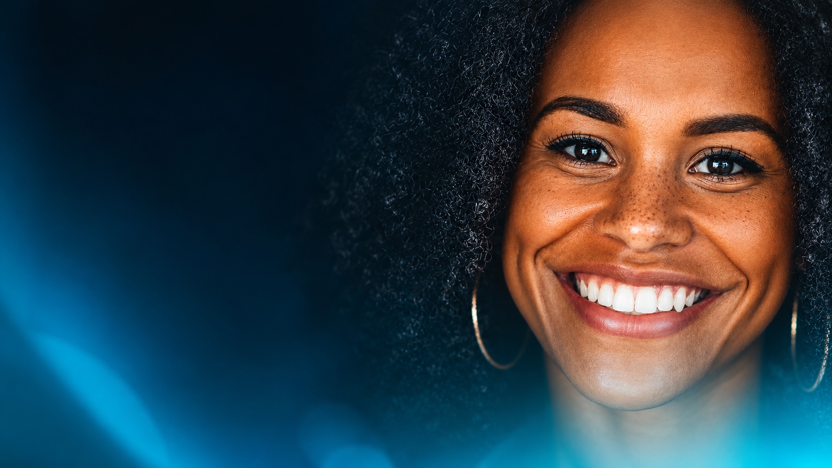 Close-up of a woman smiling joyfully, bathed in the deep blue glow of the ACTEON key visual